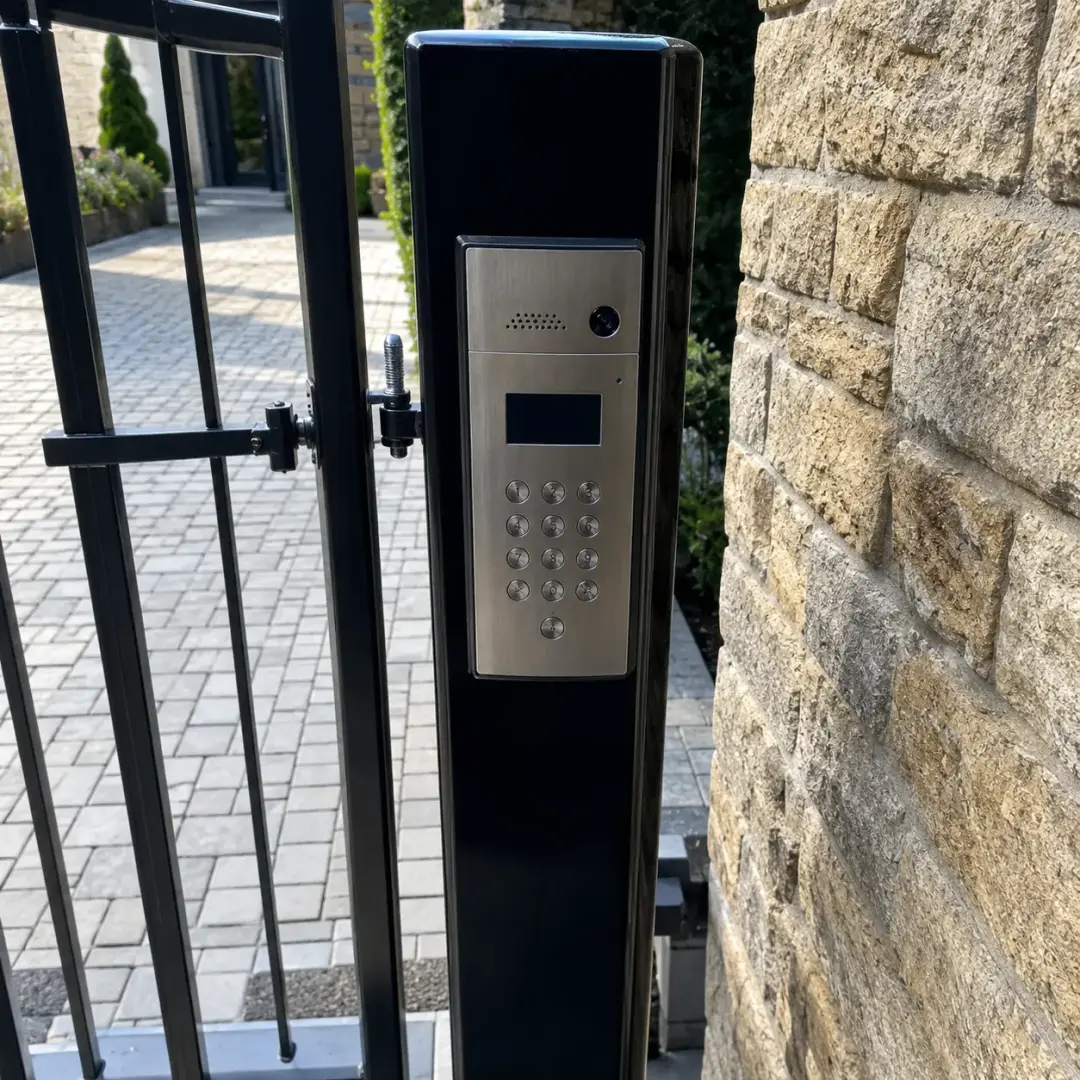 Video intercom keypad on a gate post beside a stone wall